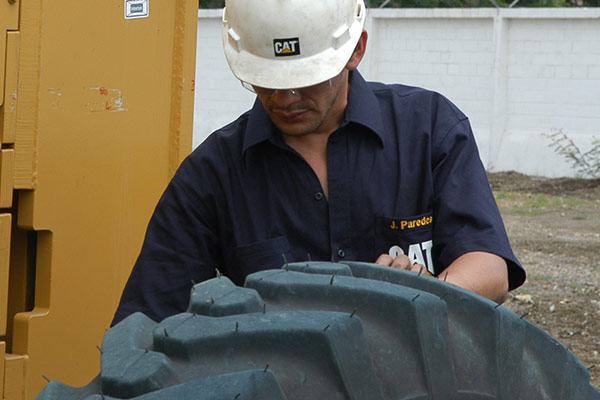Worker with Cat shirt and construction helmet inspecting a large tire